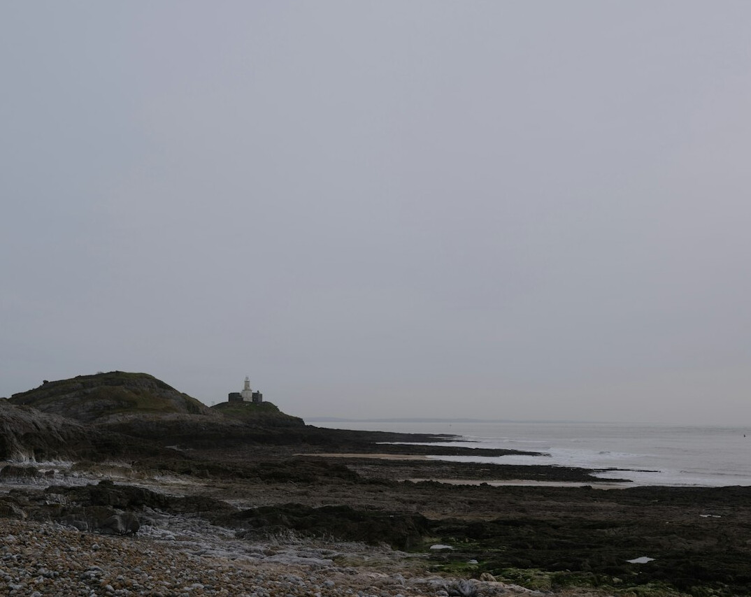 Lighthouse on a rocky coastline at dusk with light fog